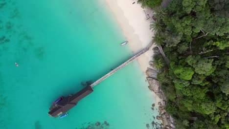 tropical-beach-with-turquoise-water,-white-sand,-and-lush-green-vegetation,-boats-anchoring-near-jetty-pier