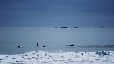 Silhouettes-of-surfers-paddling-in-the-Atlantic-Ocean-on-their-surfboards-at-Nantasket-Beach-in-Hull,-Massachusetts-USA