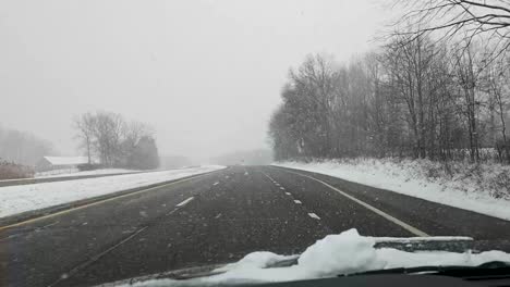 A-footage-of-vehicle-driving-on-a-snow-covered-highway-during-a-winter-snowfall,-capturing-the-cold-and-serene-landscape