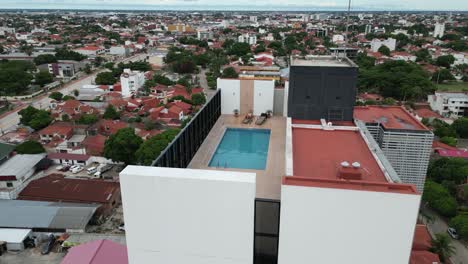 Aerial-pulls-back:-Woman-sitting-by-rooftop-swimming-pool-on-highrise