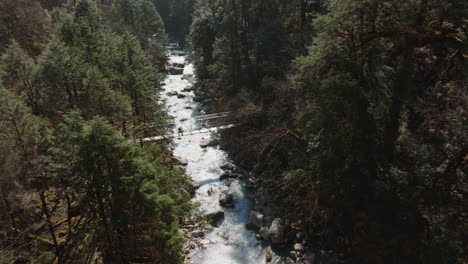 Drone-shot-captures-bridge-rivers-and-trees-in-Langtang-National-Park-trekker-hikes-in-landscape-trekking-trails-stunning-views-adding-to-breathtaking-scenery-amid-forest