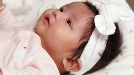 Pursing-her-lips-while-stretching-her-arms-and-looking-up,-while-lying-on-a-comfortable-mattress-in-a-crib