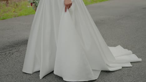 bride-in-white-wedding-gown-holding-bouquet-on-a-road,-highlighting-dress-details