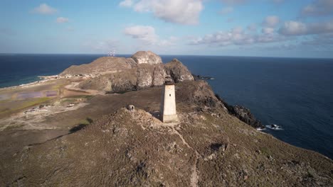 An-isolated-lighthouse-atop-a-rocky-hill-overlooking-the-ocean-during-sunrise-,-aerial-view