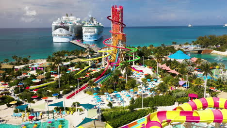 Cinematic-arial-shot-of-CoCoCay-island-with-water-slides-and-a-Royal-Caribbean-cruise-ship-in-the-background,-quickly-tilting-upward