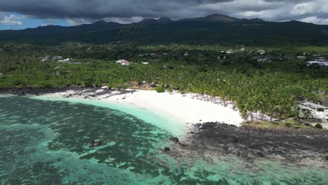 Aerial-view-of-a-tropical-beach-with-palm-trees,-white-sand,-and-volcanic-rocks