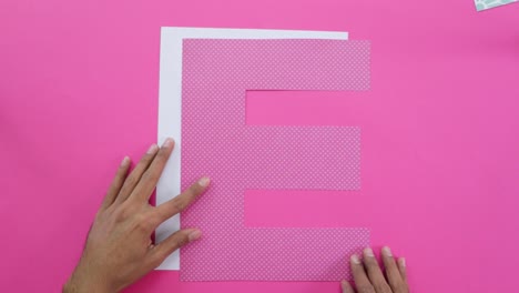 Aligning-letter-E-cutouts-from-decorated-paper-on-pink-tablecloth