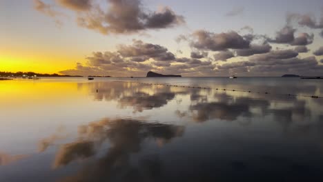 A-beautiful-upward-reveal-over-the-glossy-sunset-tainted-sea-water-finishing-on-Gunner's-Quoin-island-standing-tall-in-the-background