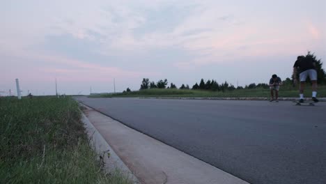 Wide-static-shot-of-friend-recording-a-male-skateboarder-failing-a-skateboard-trick-on-an-empty-road