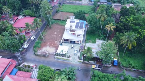 Arial-view-of-a-beautiful-Indian-Kerala-new-home,-village,-Solar-panels-in-roof-,-solar-energy-,-trees,-coconut-tree,-mountains,-grass-field,-flooded-pocket-roads,-small-town-in-Kerala