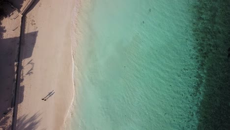 Two-people-walking-on-beach,-shadow-cast-on-sand