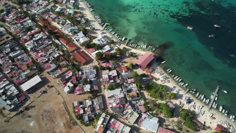 Gran-roque,-los-roques,-showing-colorful-town,-turquoise-waters,-and-a-beachside-pier,-aerial-view