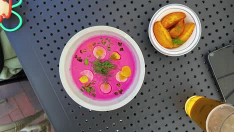 Top-view-of-a-vibrant-pink-cold-beet-soup-garnished-with-herbs-and-served-with-a-side-of-potato-wedges