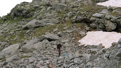 A-hiker-ascends-through-rocky-terrain-near-the-Fellaria-Glacier-in-Valmalenco,-Alps