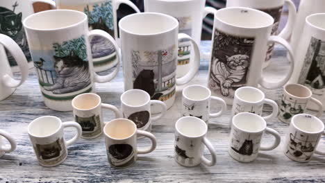 Assorted-ceramic-mugs-with-cat-illustrations-displayed-on-a-wooden-surface