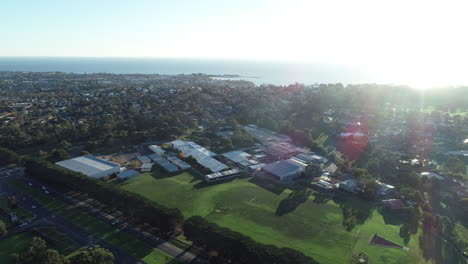 Smooth-orbit-and-approach-over-Mornington-high-school-showing-traffic-moving-along-highway-and-suburbans-and-ocean-in-the-backgorund