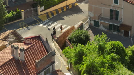 Friends-walking-down-a-narrow-street-in-Lorenzana-Italy-during-a-sunny-day,-aerial-view