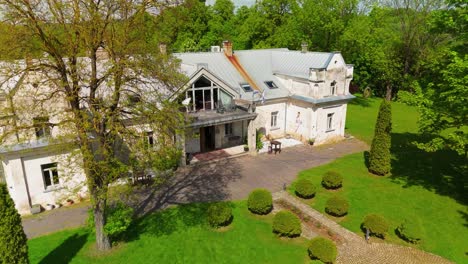 Aerial-view-of-Babtyno-Manor,-a-historic-estate-surrounded-by-lush-greenery,-featuring-classic-architecture-and-a-well-kept-garden