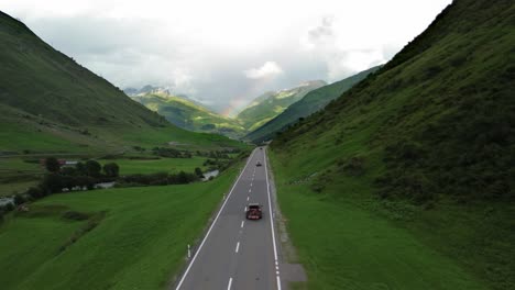 Road-in-Swiss-Alps-with-cars-and-rainbow-at-the-sky-shot-from-a-drone