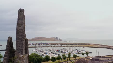 Drone-ascends-along-broken-exposed-walls-and-facade-of-Howth-Abbey-to-reveal-Ireland's-Eye