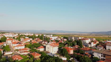 Establishing-drone-shot-of-a-small-town-on-a-clear-summer-day,-with-houses-with-red-roods-and-lots-of-trees-between-the-buildings