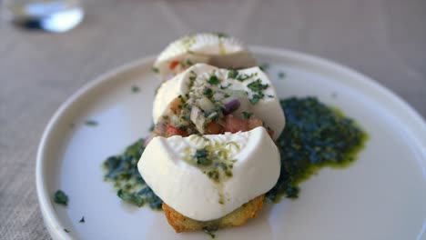 Slow-motion-footage-showing-a-plate-of-bruschetta-topped-with-Gozo-cheese,-chopped-tomatoes,-onions-and-pesto