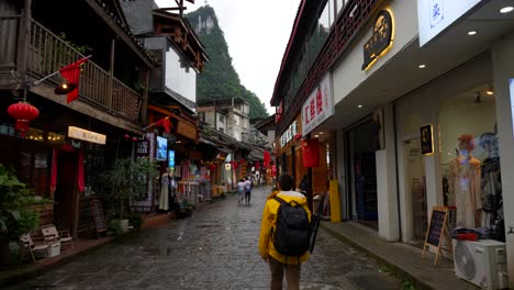 Tourist-walking-with-photography-gear-on-Xingping-ancient-street,-Laozhai-Hill-in-background