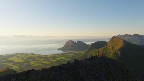 Man-lift-arms-cheering-on-Norway-mountain-top-with-majestic-coastal-view