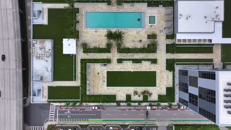 Ascending-top-down-shot-of-high-rise-residential-complex-with-private-swimming-pool-near-Highway-of-Miami-City,USA