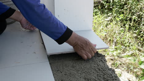 A-construction-worker-puts-a-tile-in-place,-on-top-of-a-freshly-mixed-mortar-then-taps-it-gently-using-a-mallet