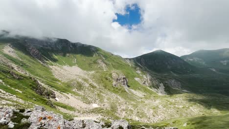 A-mountain-landscape-featuring-rocky-slopes,-grassy-areas-under-a-cloudy-sky