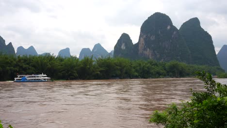 Cruise-ship-navigates-Lijiang-river-brown-waters-along-karst-mountains-in-Xingping,-China