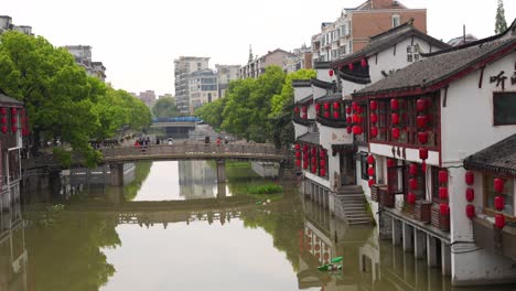 Chinese-houses-with-red-lanterns-next-to-a-bridge-over-a-canal-in-Qibao-Ancient-Town,-China