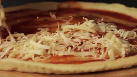 Un-Primer-Plano-De-Queso-Rallado-Que-Se-Coloca-Sobre-Una-Masa-De-Pizza-Con-Salsa-De-Tomate,-Lo-Que-Resalta-El-Proceso-De-Preparación-De-La-Pizza-Casera.