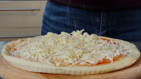 Sprinkling-oregano-on-a-freshly-prepared-pizza-topped-with-grated-cheese