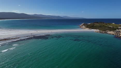 White-sand-beach-with-walking-tourists-at-sandbar-revealing-Diamond-Island,-aerial-dynamic