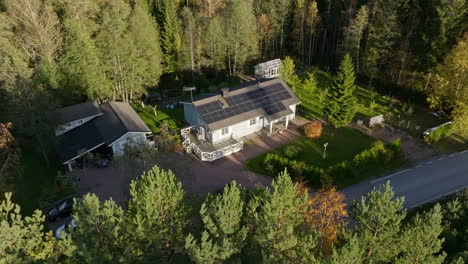 Drone-circling-in-front-of-a-solar-house-in-middle-of-sunlit-autumn-color-forest