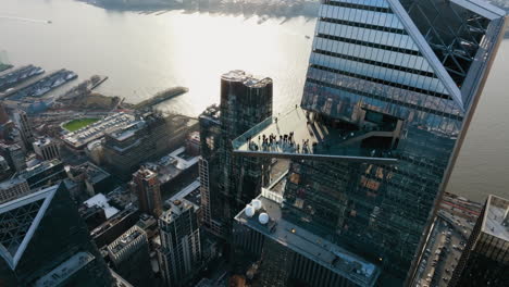 Aerial-view-tilting-over-people-on-the-Edge-skydeck-of-the-North-tower-in-sunny-Hudson-Yards,-New-York