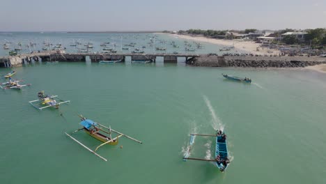 Aerial-view-of-Indonesian-traditional-juking-boat-departing-to-the-sea-from-the-beach-on-turquoise-transparent-waves-near-a-tropical-island-of-Bali