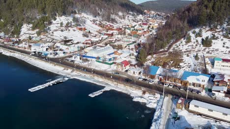 Witness-the-stunning-frozen-landscape-of-Lake-Baikal-in-Siberia,-showcasing-a-picturesque-jetty-and-the-tranquil-charm-of-winter-in-the-surrounding-town