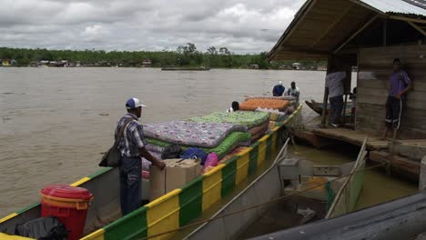 Mattresses-being-loaded-onto-a-long-river-boat-on-the-shore-of-a-large-river