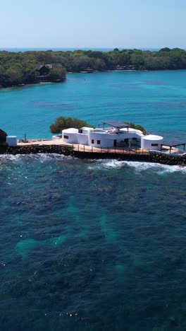 Toma-Vertical-Con-Dron-De-Una-Casa-Blanca-En-Una-Pequeña-Isla-Del-Mar-Caribe