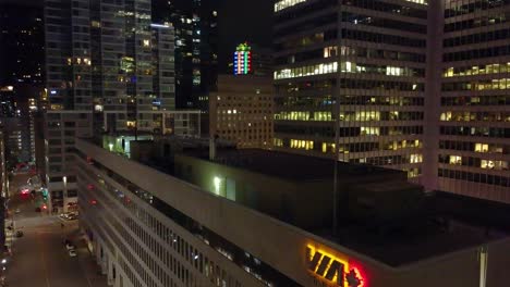 Drone-flies-above-stunning-glass-buildings-with-the-Via-logo-at-night,-with-city-lights-in-Montreal,-Canada