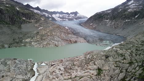 Rhone-Glacier-at-Furka-Pass-in-Switzerland-during-cloudy-day-with-lake-shot-from-a-drone