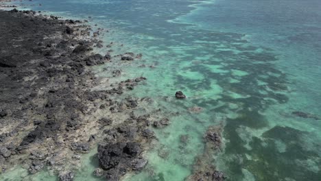 Aerial-view-of-rocky-volcanic-coastline-meeting-clear-turquoise-ocean-waters