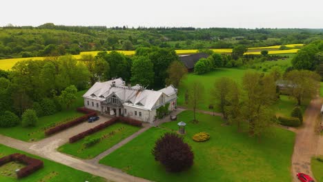 Vista-Aérea-De-La-Mansión-Babtyno,-Una-Finca-Histórica-Rodeada-De-Exuberante-Vegetación,-Con-Arquitectura-Clásica-Y-Un-Jardín-Bien-Cuidado.