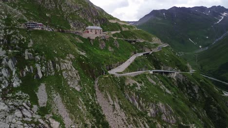 Furka-Pass-in-Switzerland-during-cloudy-day-with-low-traffic-and-iconic-hotel-shot-from-a-drone