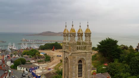 Aerial-dolly-to-gilded-gold-spires-on-tower-of-Church-of-the-Assumption-in-Howth-North-Dublin-Ireland-with-Ireland's-eye-off-coast