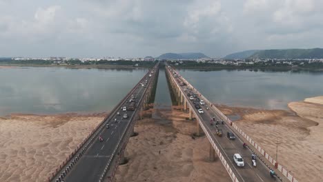 This-aerial-video-captures-the-city's-bustling-urban-landscape,-where-the-majestic-Krishna-River-flows-beneath-the-intersecting-Chennai-Kolkata-Highway-bridge,-bustling-with-vehicular-traffic