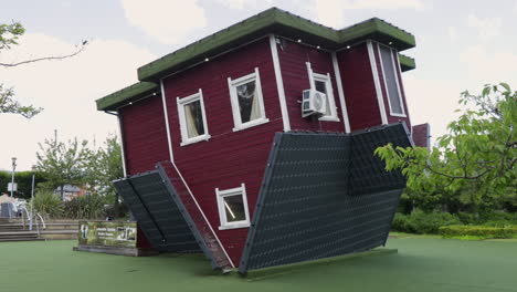 Upside-down-red-house-with-white-trim-and-green-roof-in-a-park-setting